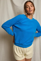 Woman wearing a blue sweater and beige shorts against a plain background