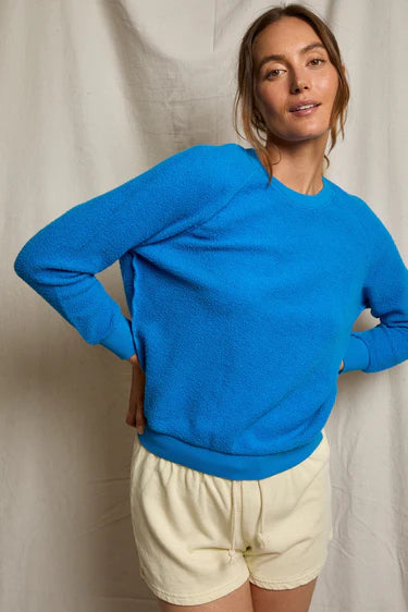 Woman wearing a blue sweater and beige shorts against a plain background