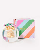 Matches in a glass holder with a colorful striped box on a white background