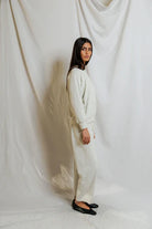 Person wearing a white outfit standing against a white curtain
