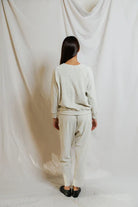 Person wearing a beige sweater and pants set against a white draped curtain background