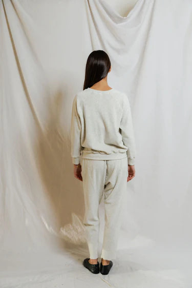 Person wearing a beige sweater and pants set against a white draped curtain background