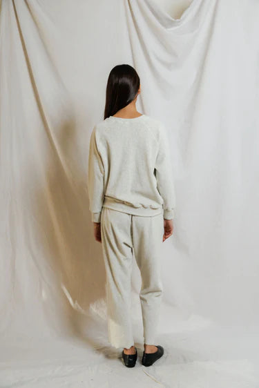 Person wearing a beige outfit standing against a white curtain.