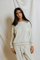 Woman wearing a light gray sweatshirt and pants against a white background