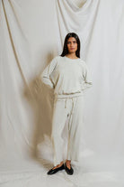 Woman wearing a white outfit standing against a white curtain.