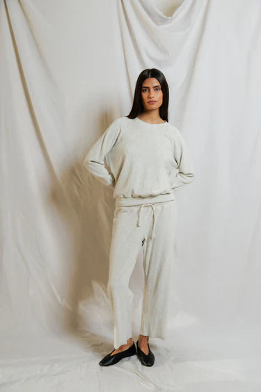 Woman wearing a white outfit standing against a white curtain.