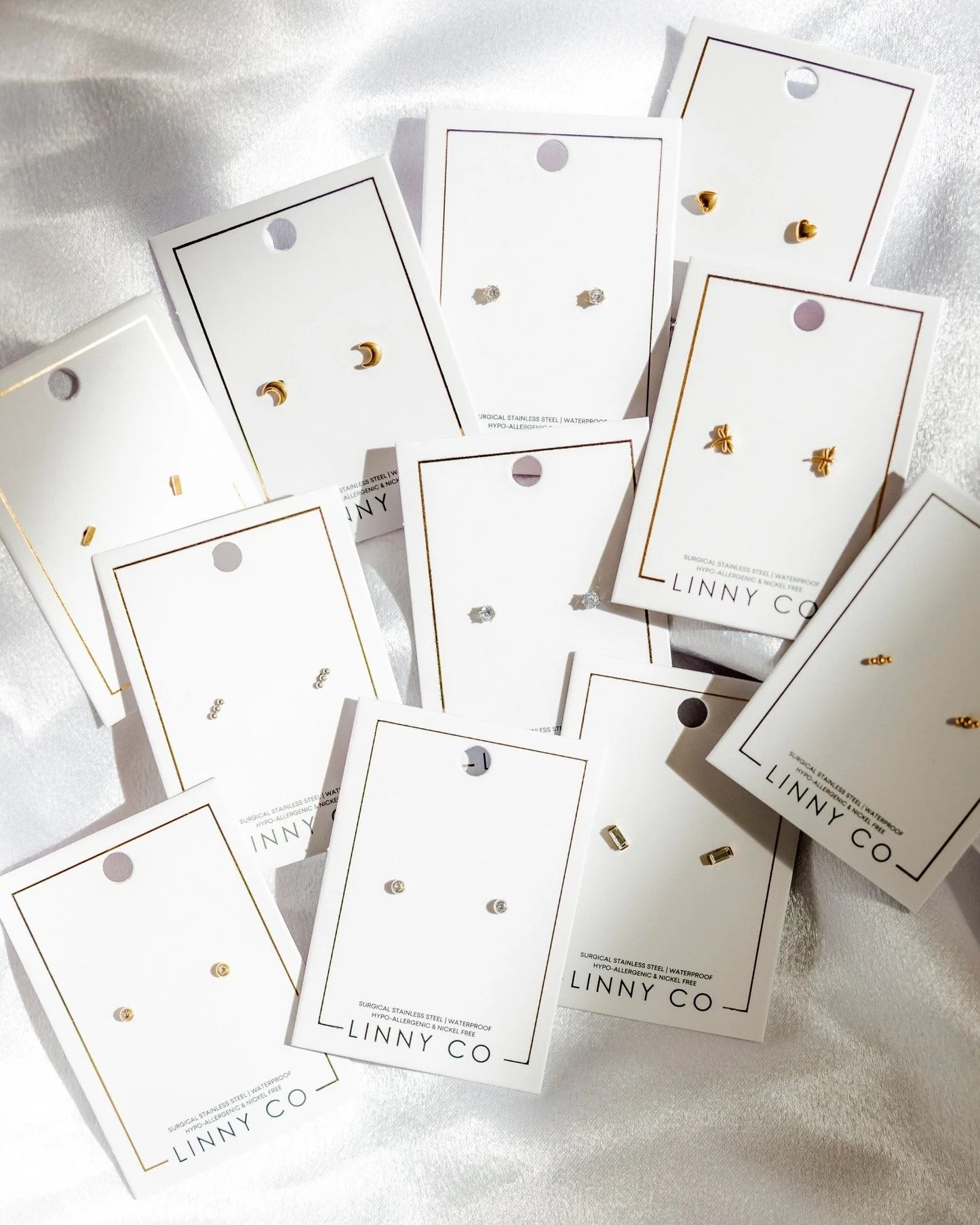 Collection of earring cards with 'LINNY CO' branding on a white fabric background