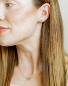 Close-up of a person wearing green bow-shaped earrings with a neutral background