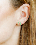 Close-up of an ear wearing a green bow-shaped earring with blonde hair.