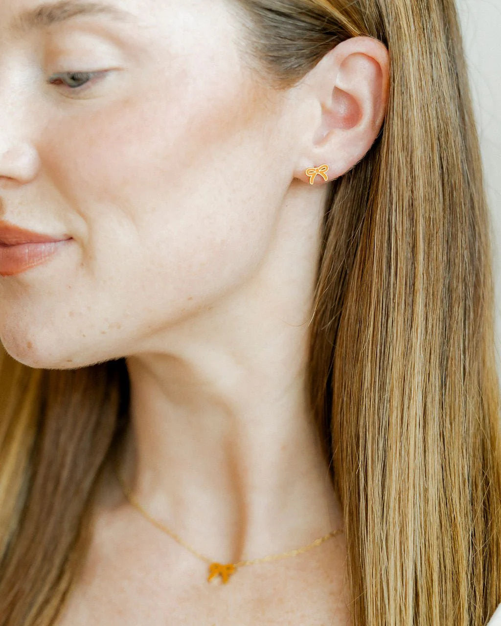 Close-up of a person wearing gold stud earrings with a plain background