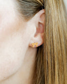 Close-up of an ear wearing a gold bow-shaped earring with hair partially covering the frame.
