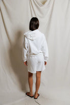 Person wearing a white robe standing against a plain white background