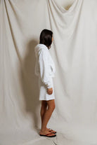 Person wearing a white hoodie standing in front of a draped white curtain
