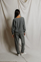 Person wearing a gray sweatshirt and pants set against a plain white background