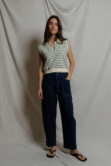 Woman wearing a striped sleeveless top and dark pants against a plain background