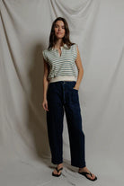 Woman wearing a striped sleeveless top and dark pants against a plain background