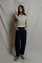 Woman wearing a striped shirt and dark pants against a plain background