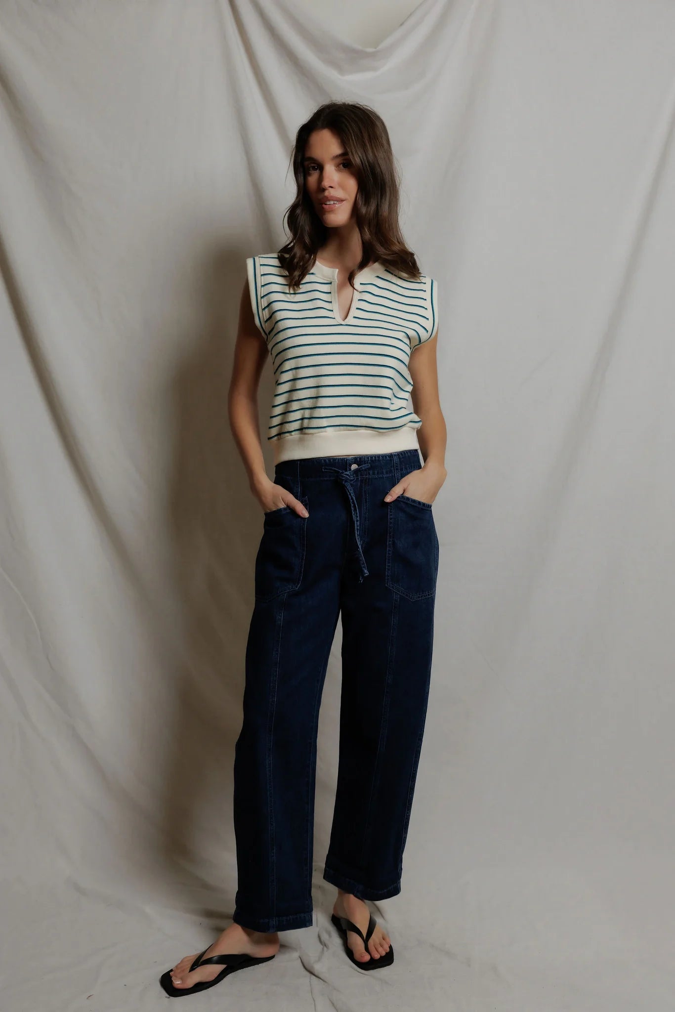 Woman wearing a striped shirt and navy pants against a plain background
