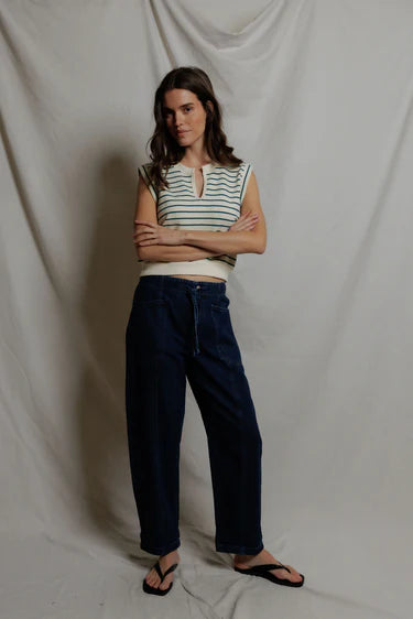 Person wearing a striped sleeveless top and dark pants against a plain background