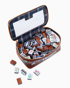 An open zippered carrying case filled with mahjong tiles, shown on a clean white background. The case has a navy blue and gray plaid interior lining, a brown exterior, and gold-toned zipper trim.