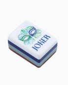 A small rectangular white box with a blue and green masquerade mask graphic and the word 'JOKER' printed in blue, shown on a plain white background.