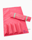 Pink travel mat with rolled-up towel and pouch on a white background