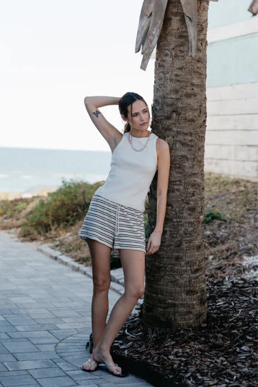 Woman leaning against a palm tree by a beachside path