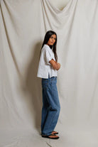 Person wearing a white shirt and blue jeans standing against a plain background