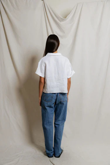 Person wearing a white shirt and blue jeans standing against a plain white backdrop