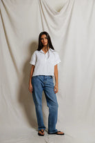 Woman wearing a white shirt and blue jeans standing against a plain background