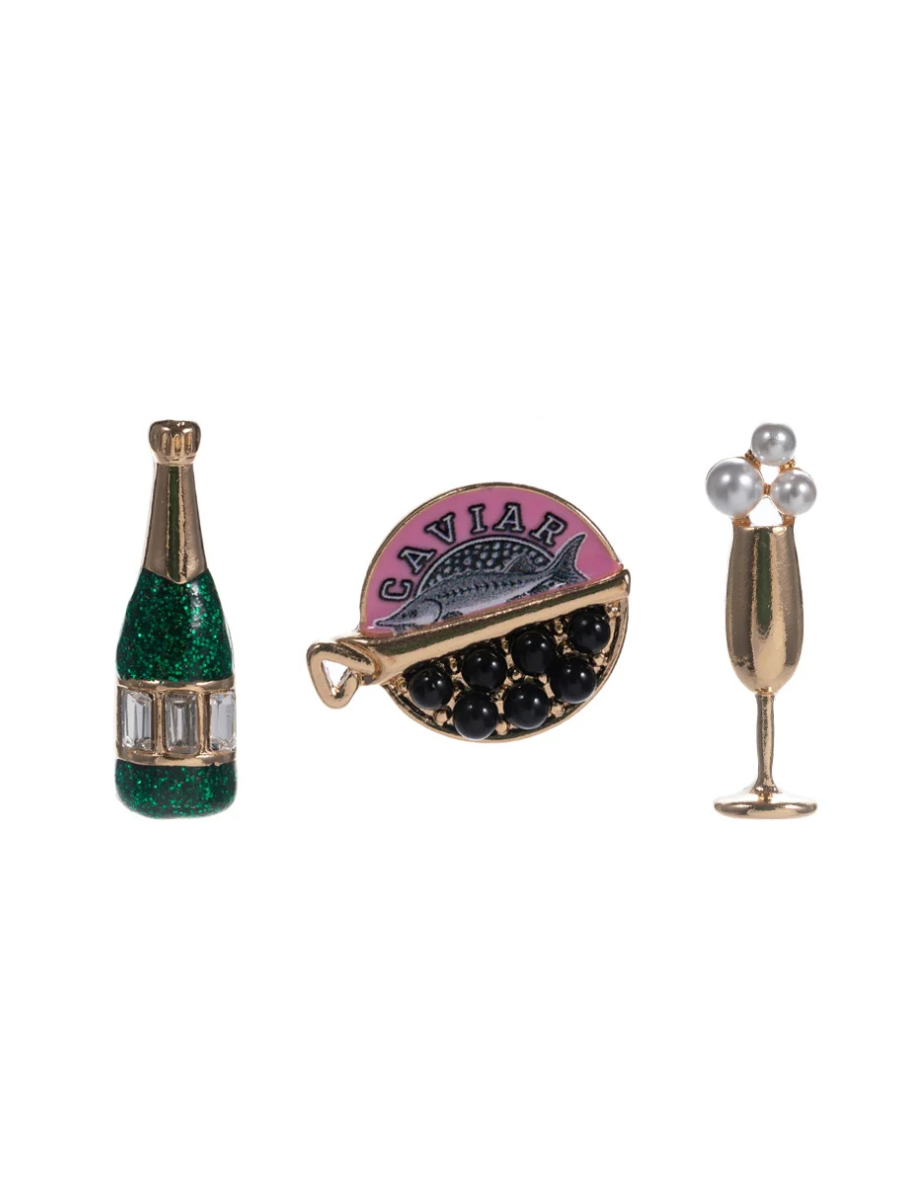 Three decorative pins shaped like a champagne bottle, a round pink and black item, and a champagne glass on a white background.