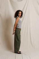 Woman wearing a striped tank top and green pants against a plain background