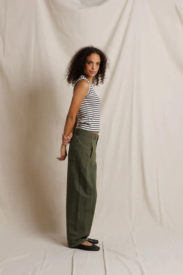 Woman wearing a striped tank top and green pants against a plain background