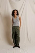 Woman wearing a striped tank top and green pants against a plain background