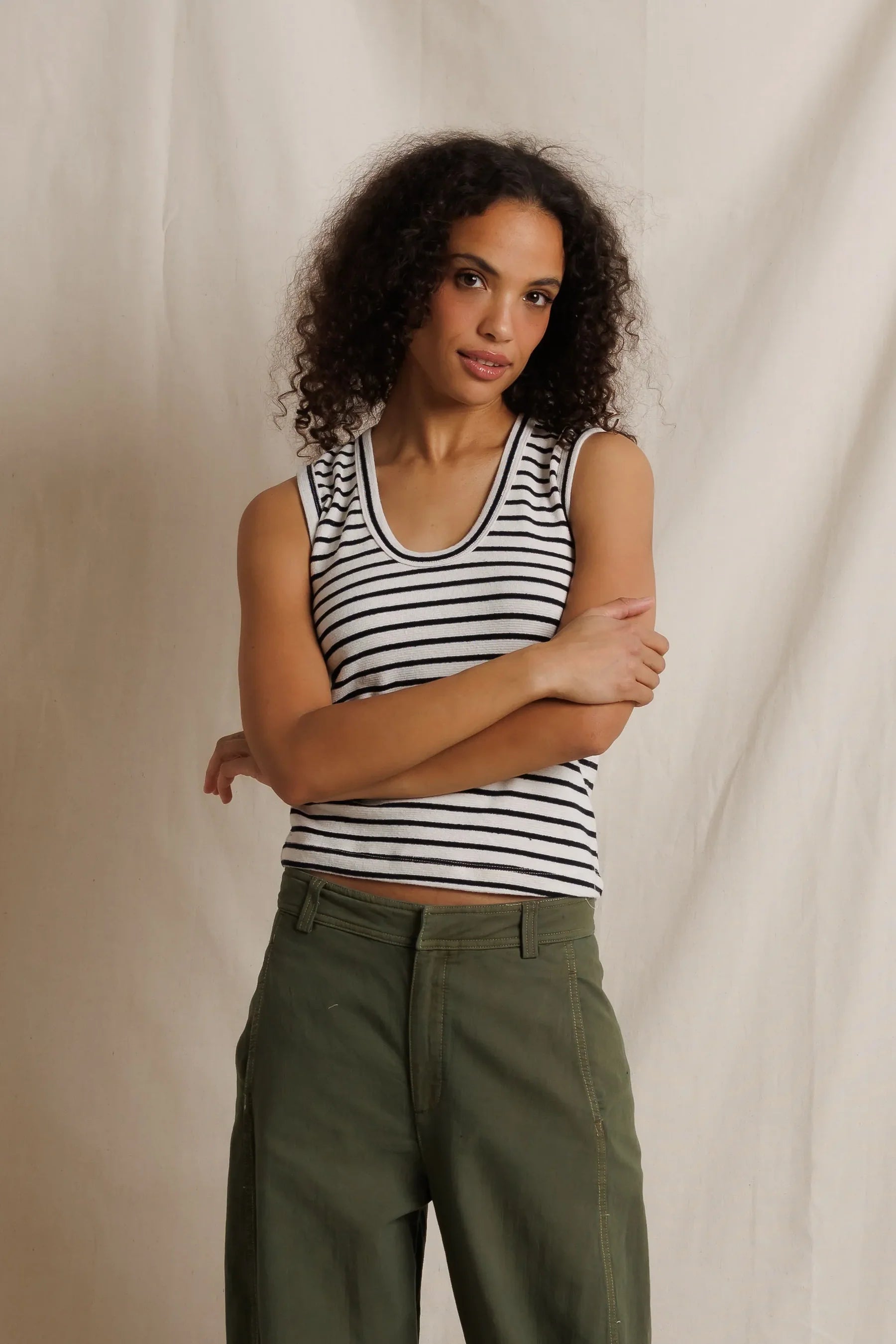 Woman wearing a striped tank top and green pants against a neutral background
