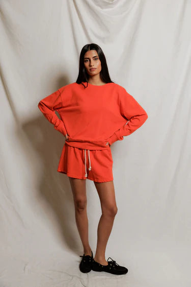 Person wearing a bright orange sweatshirt and shorts set against a plain background
