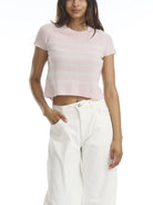Woman wearing a light pink cropped top and white pants on a white background