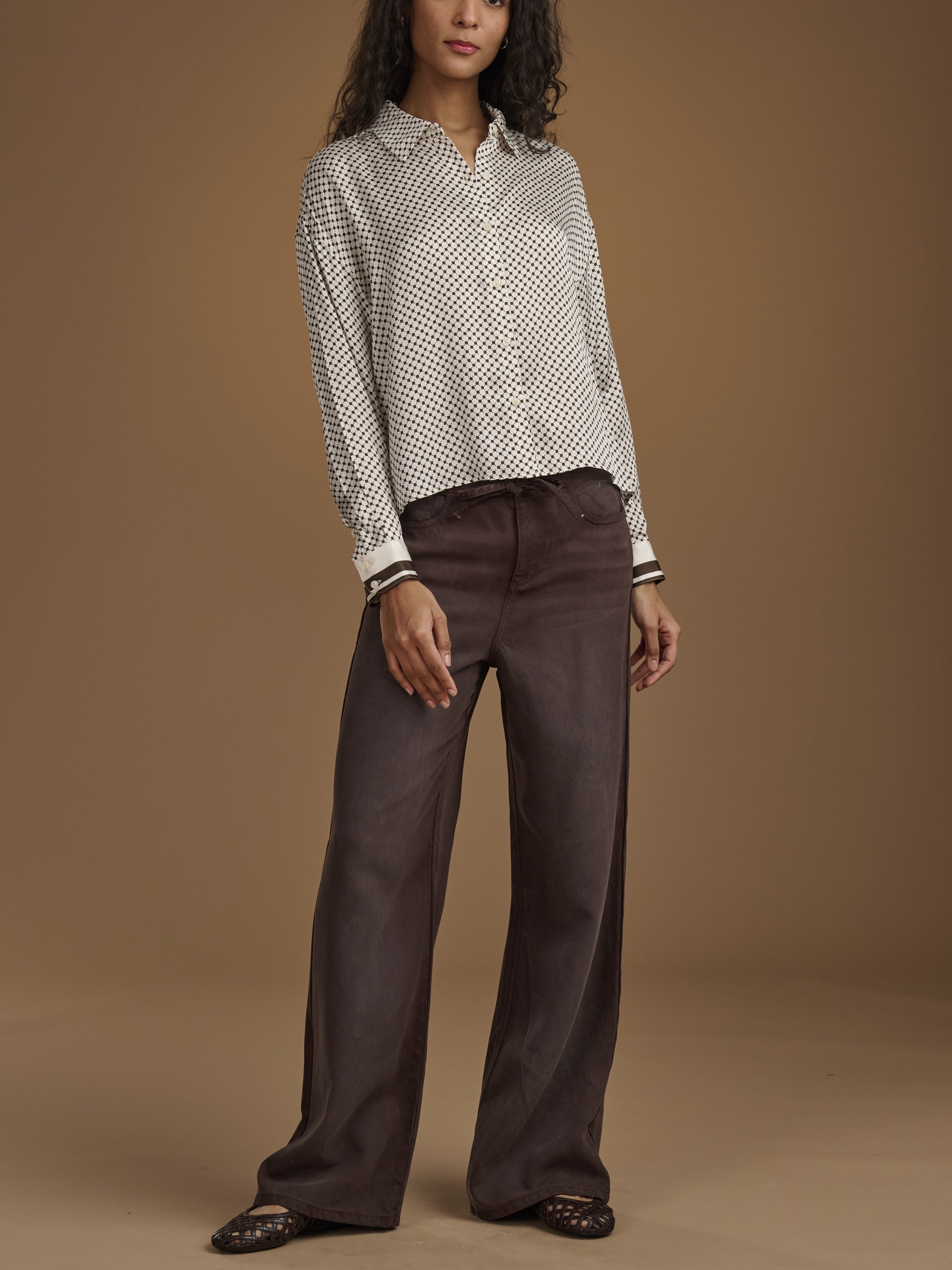 Woman wearing a patterned blouse and brown pants on a brown background