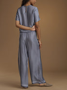 A woman shown from the back wearing a matching short-sleeve top and wide-leg pants set in a blue and white micro-pattern, against a solid tan studio background.