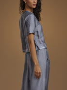 A woman shown from the back wearing a matching short-sleeve top and wide-leg skirt set in a blue and white geometric pattern, set against a solid warm brown studio background.