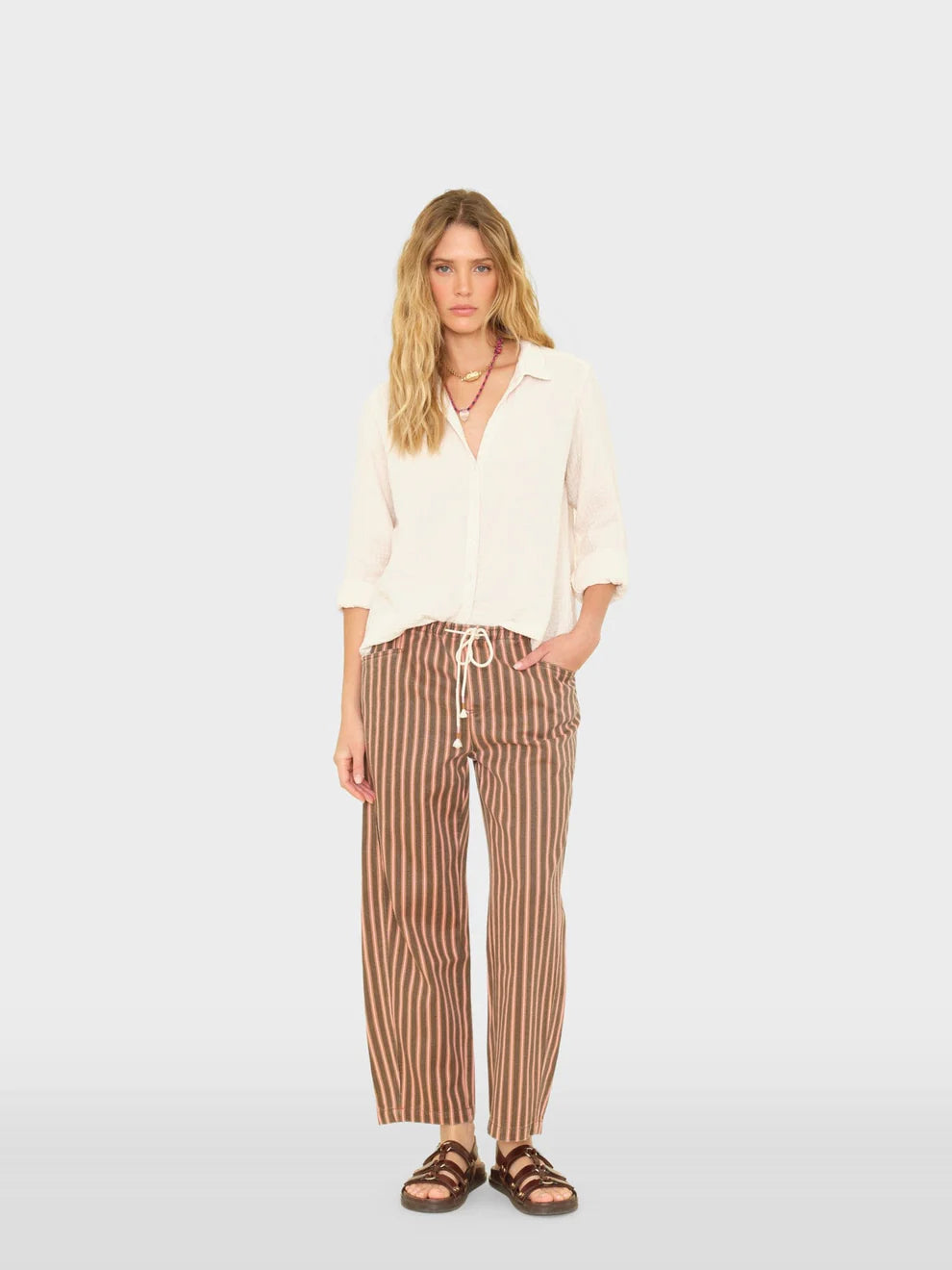 Woman wearing a white blouse and striped pants on a light gray background