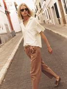 Woman walking on a street wearing a white blouse and brown pants.