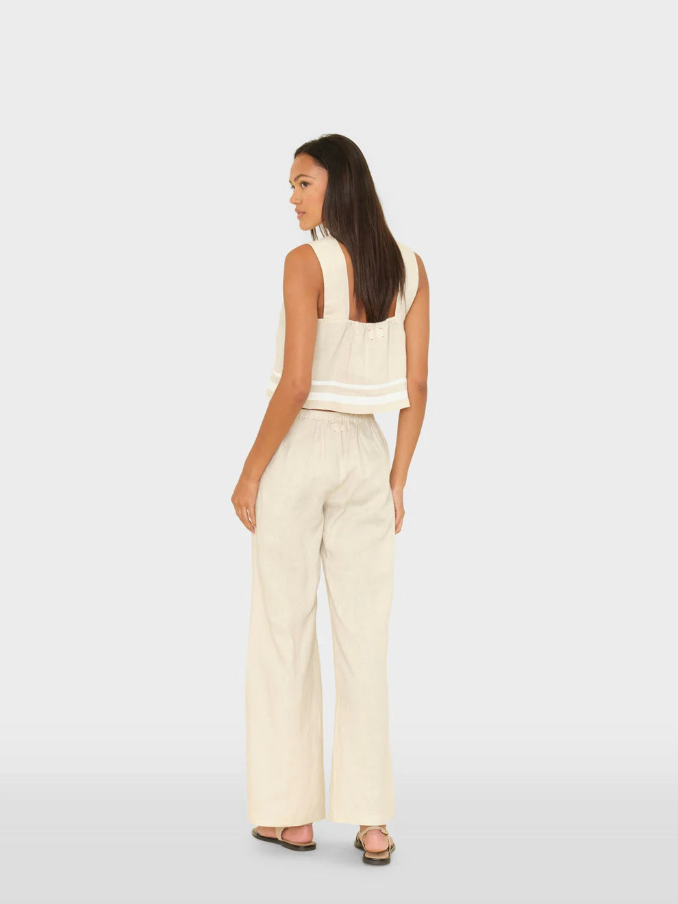 Woman wearing a white sleeveless top and cream-colored pants on a light gray background