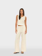 Woman wearing a white sleeveless top and wide-leg pants on a light gray background