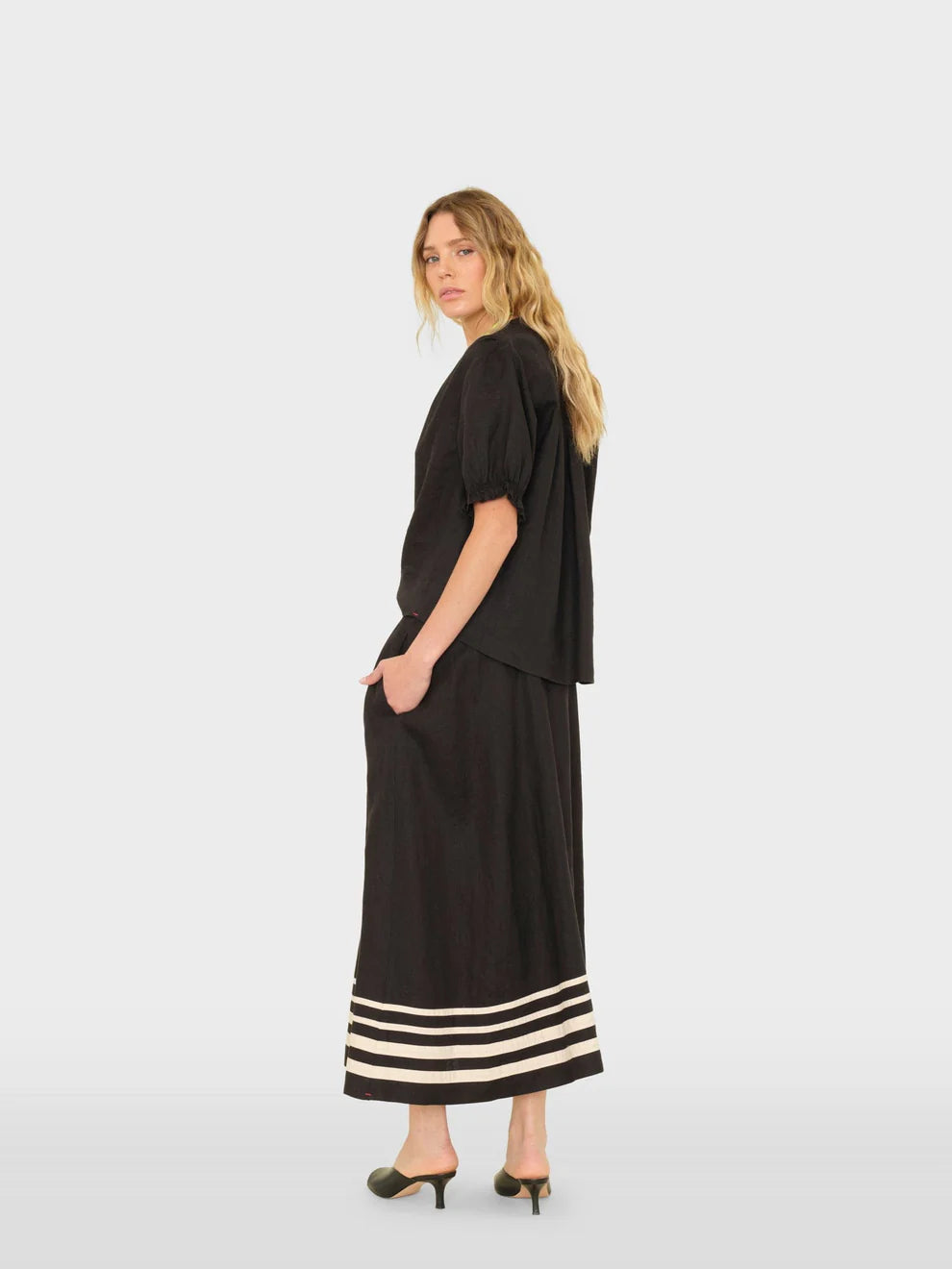 Woman wearing a black outfit with a long skirt and striped hem on a white background