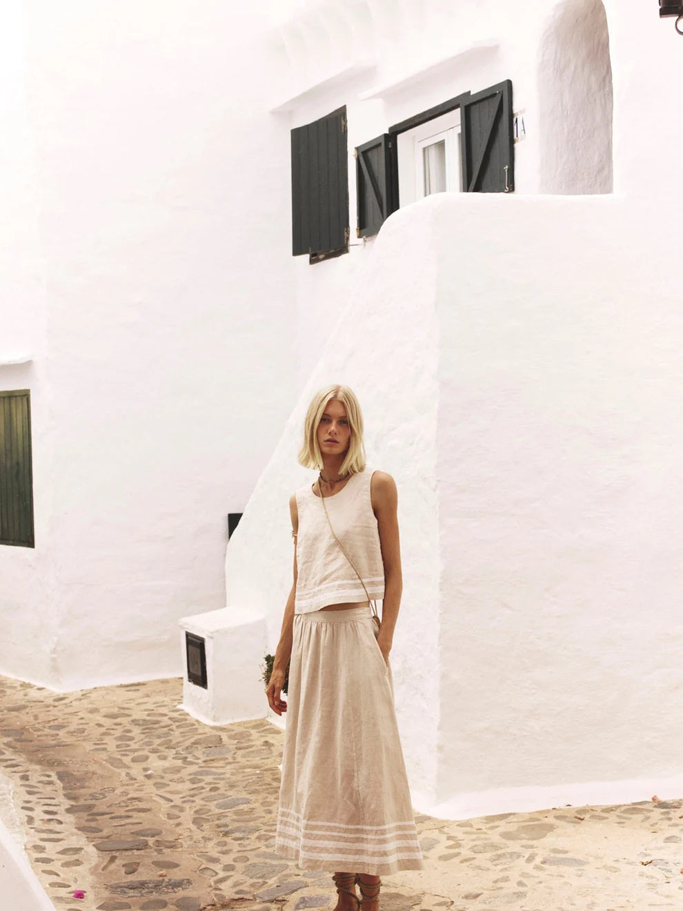 Woman in a white dress standing in front of a white building with black shutters.