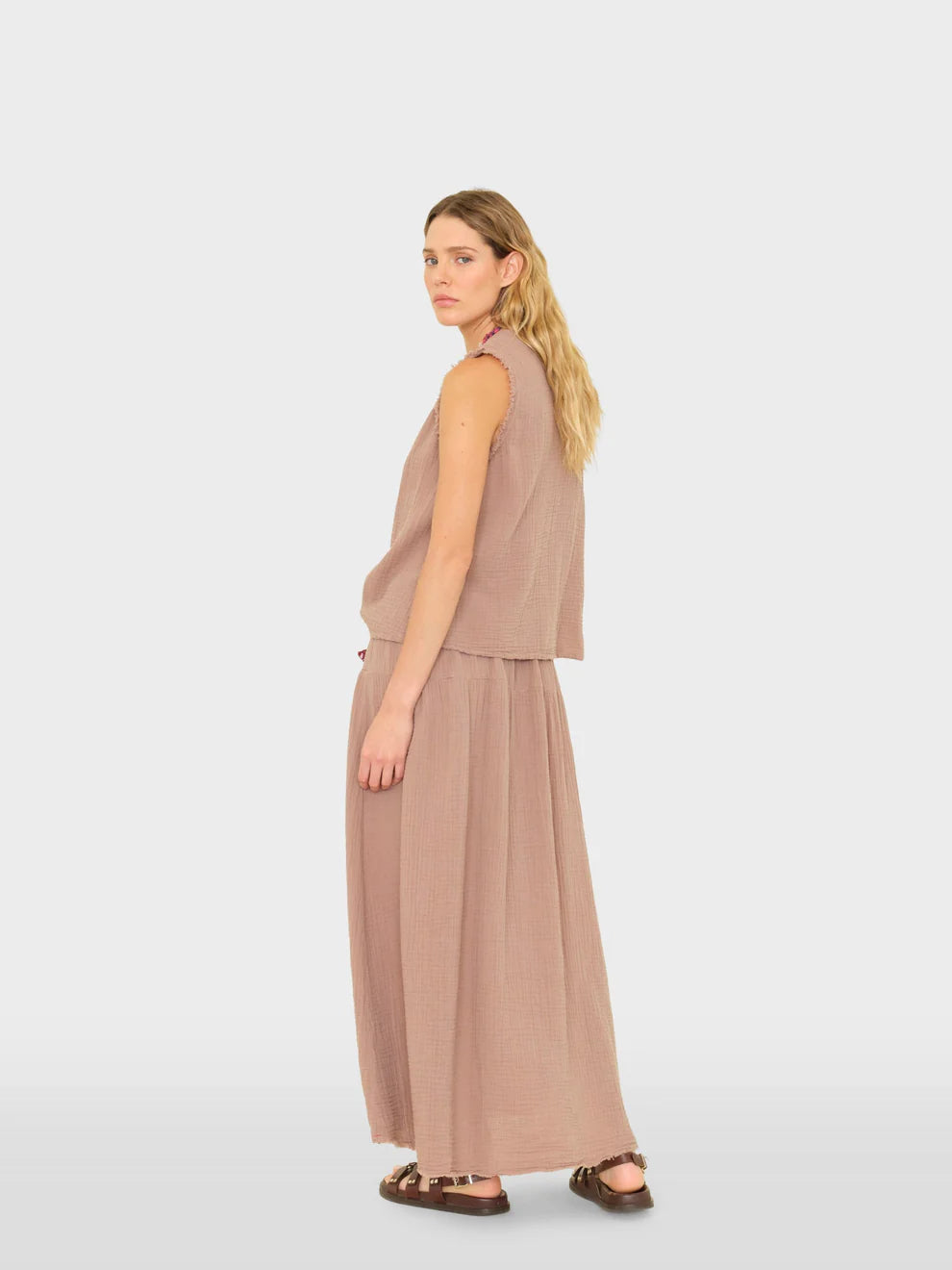 Woman wearing a beige sleeveless top and long skirt on a white background