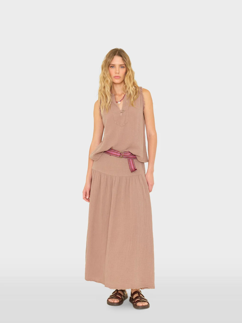 Woman wearing a beige sleeveless top and long skirt with a red belt on a white background