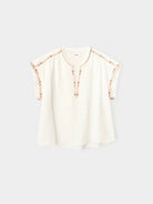 White blouse with floral embellishments on a light gray background
