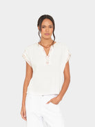 Woman wearing a white blouse with lace details on a plain background